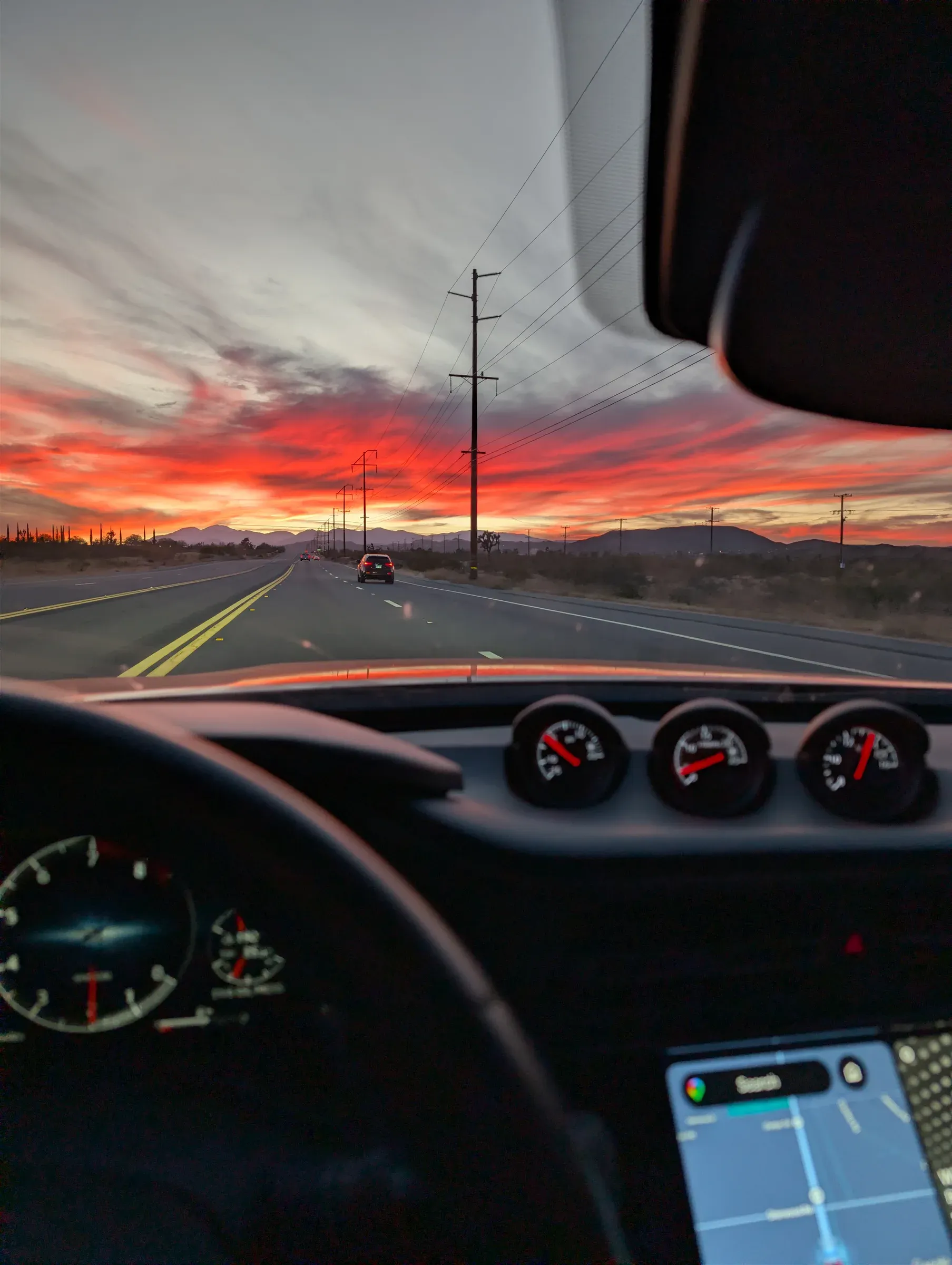 A red sunset over a desert highway, seen from behind the wheel of a car