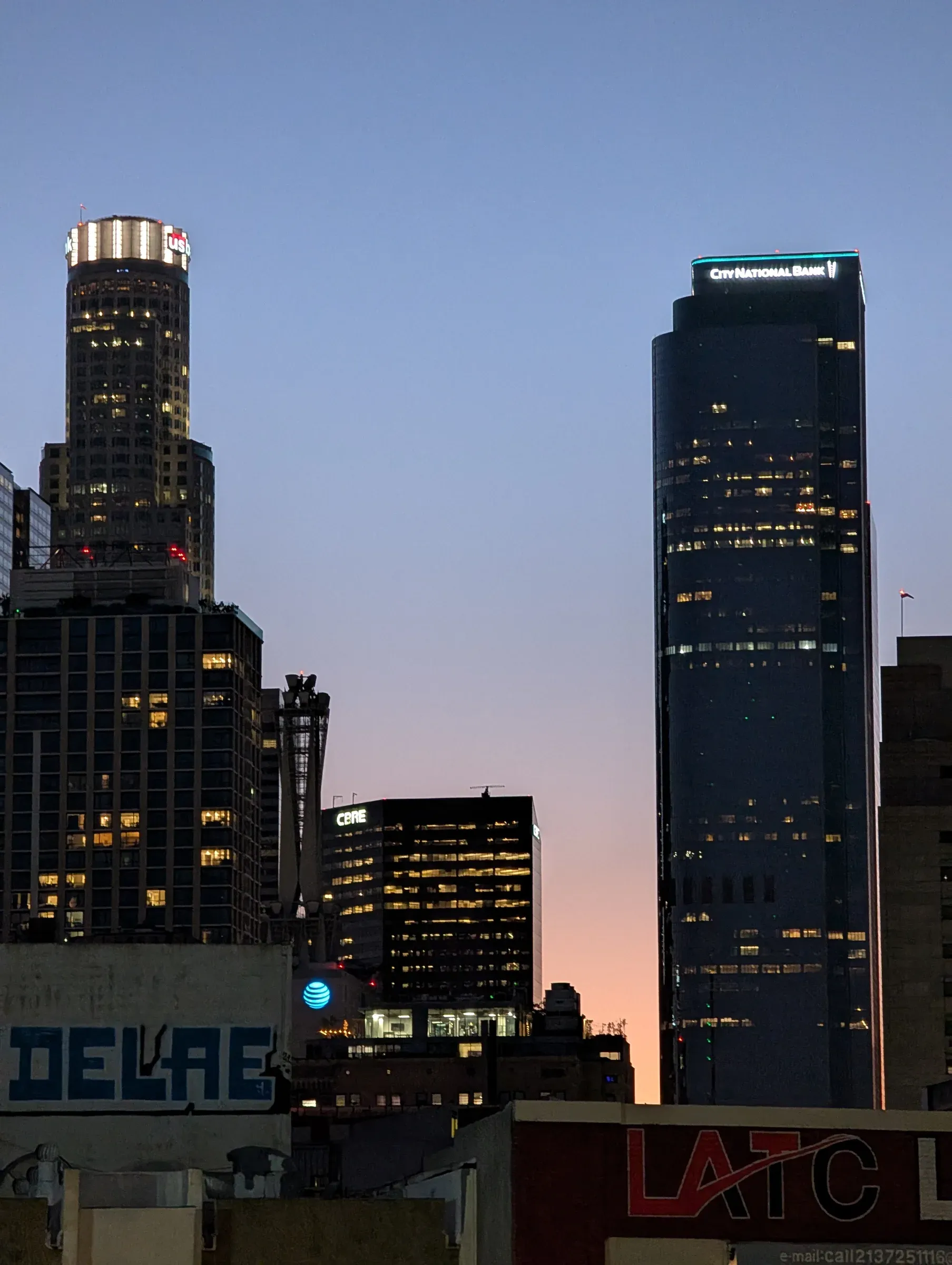Downtown Los Angeles towers lit up at dusk, with a sliver of pink sky between them