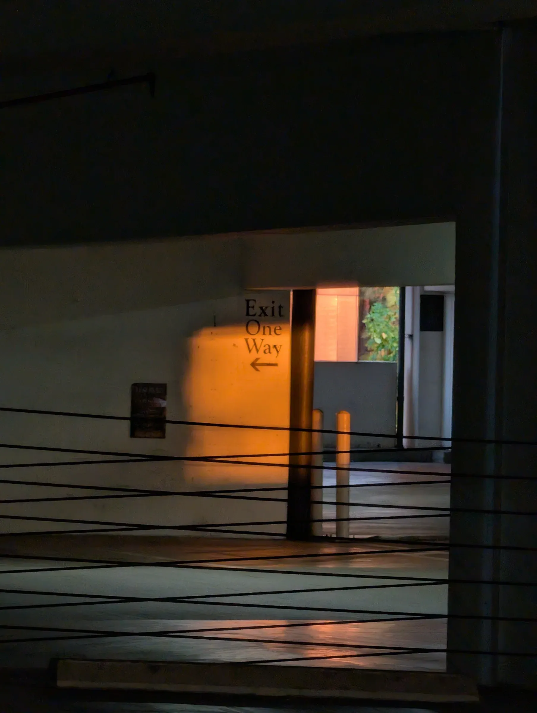 A dark parking garage with an Exit One Way sign lit by warm orange light