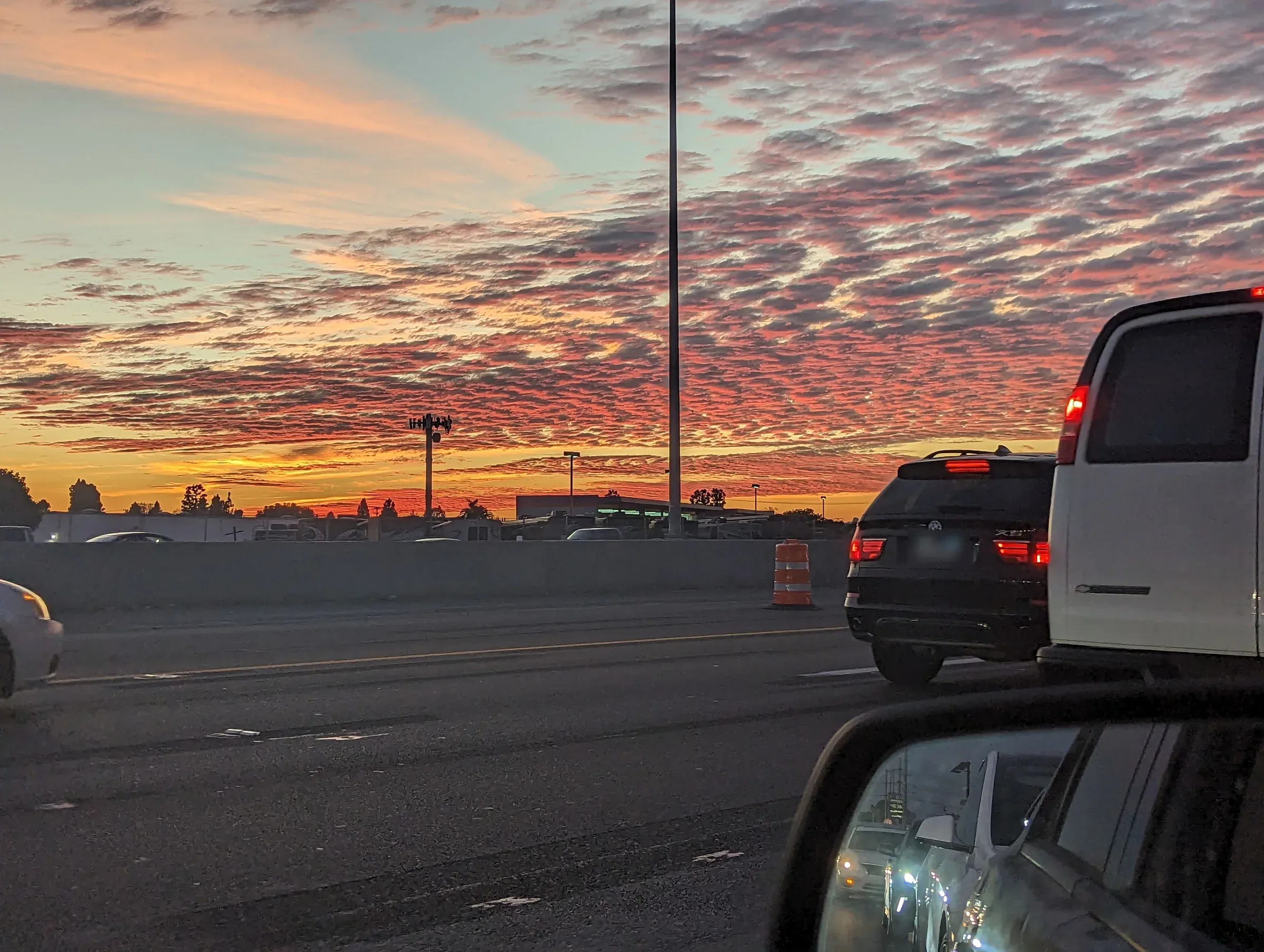 Rippled pink clouds over a freeway at sunset, seen from a car in traffic
