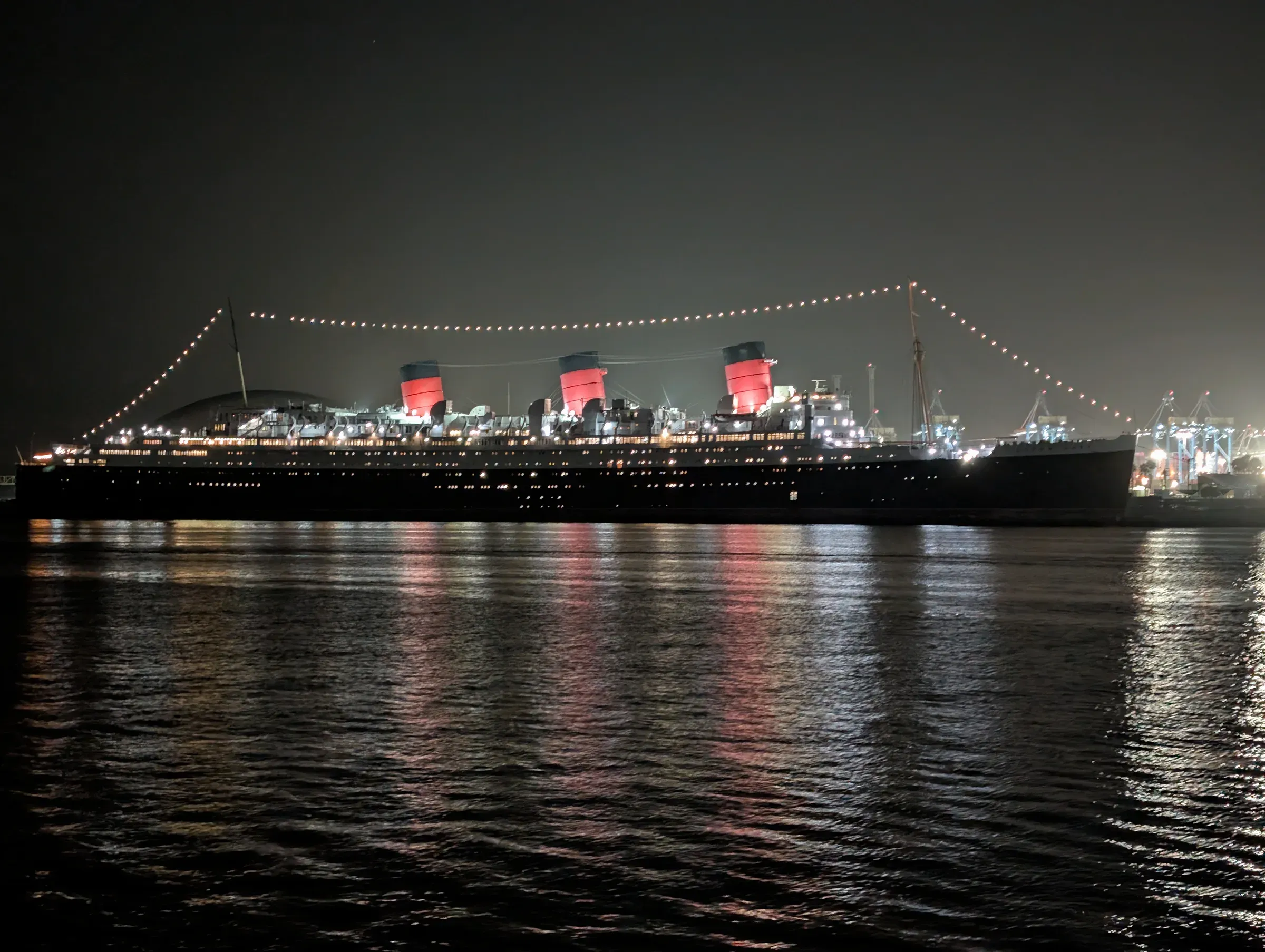 The Queen Mary lit up at night, its lights reflected in the water